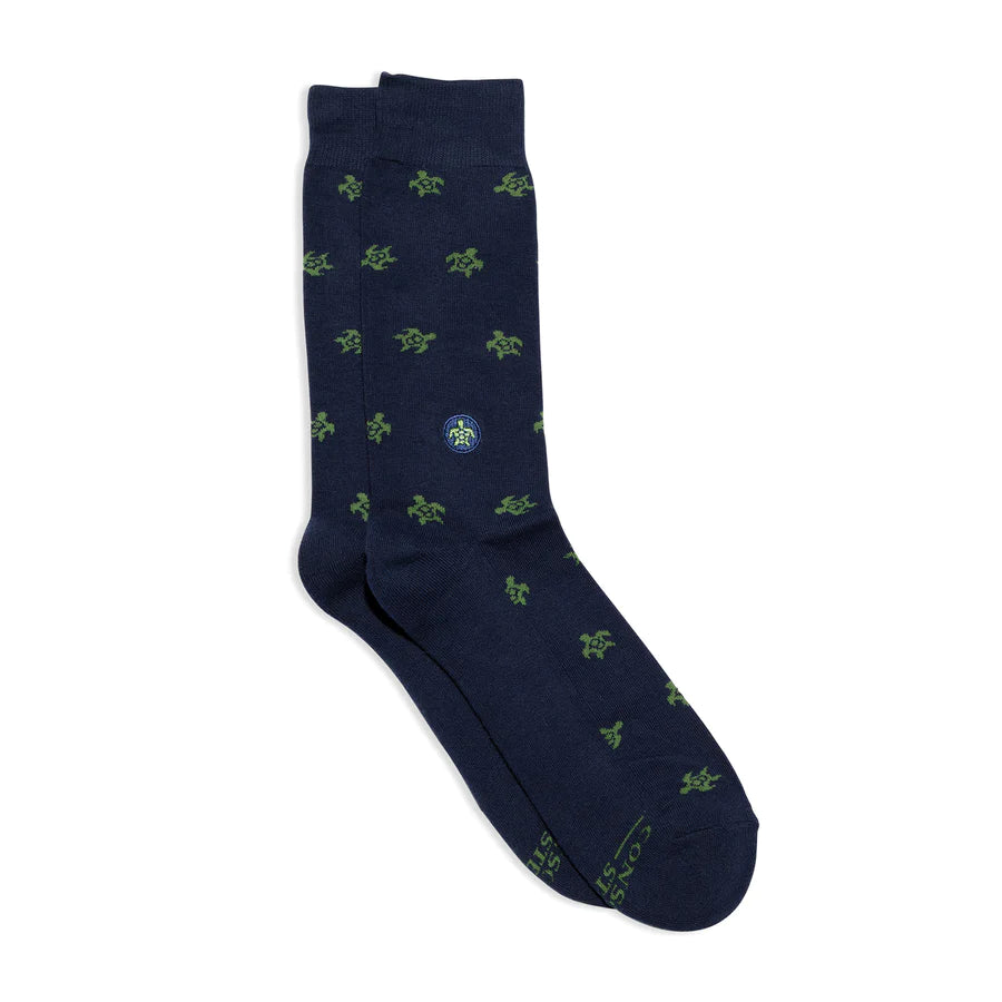 A pair of dark blue Conscious Step socks with a green sea turtle pattern is shown against a white background. The brand name is visible on the bottom of the socks.