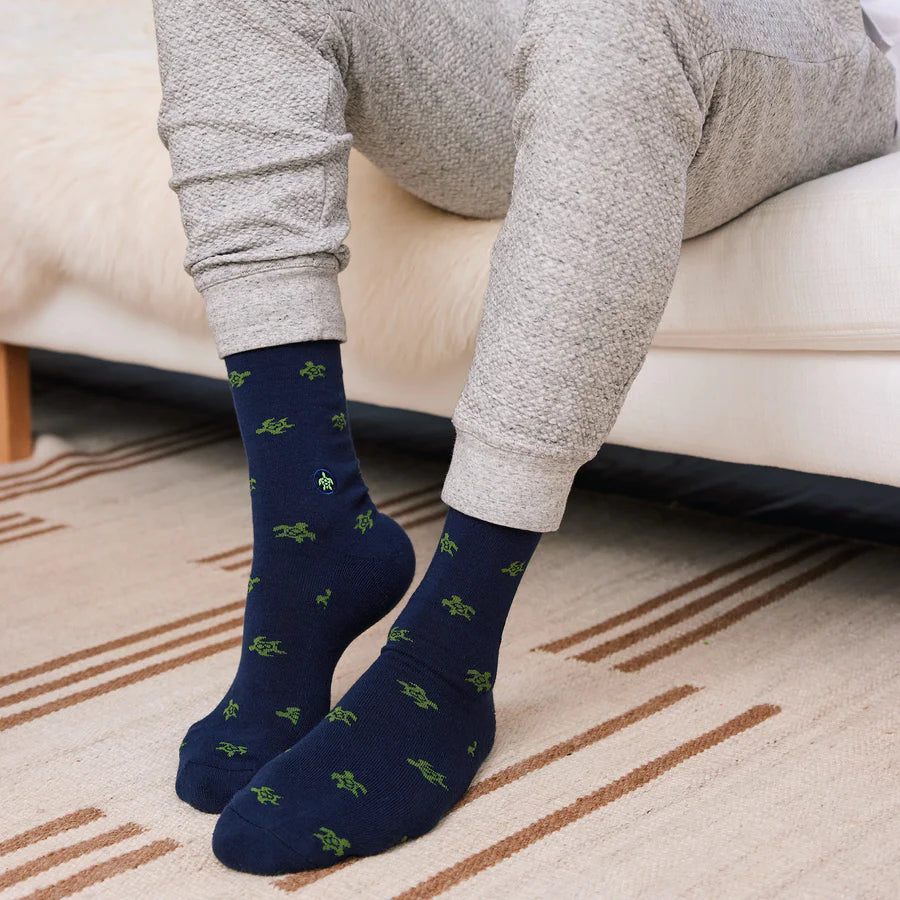 A person is shown wearing gray pants and dark blue socks with a green sea turtle pattern, seated on a couch.