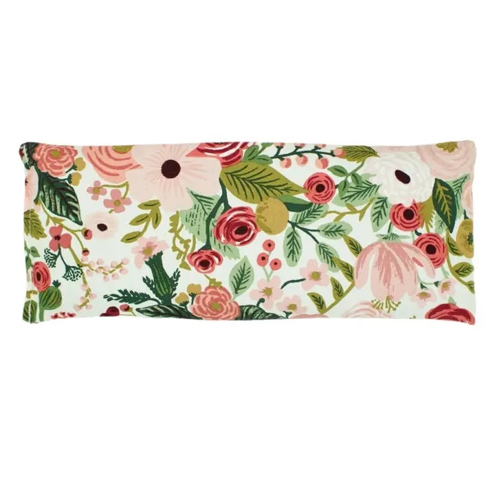 An eye pillow with a vibrant floral pattern features large pink and red flowers with bright green leaves and small berries.