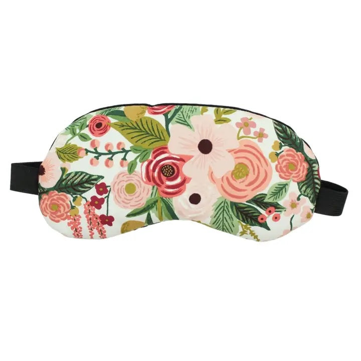 A handmade cotton eye mask with a white background is shown. The mask features a pattern of pink, red and green flowers, it has a black elastic band.