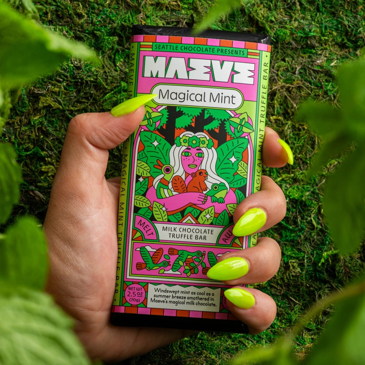 A hand holding a Maeve “Melt Away Mint” truffle bar outdoors, with green grass in the background, capturing a fresh, natural setting for the chocolate treat.