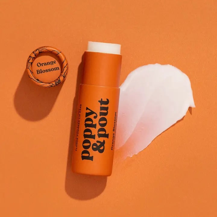 Orange Blossom lip balm by Poppy & Pout, displayed against a pale backdrop with citrus tones complementing its soft orange packaging.