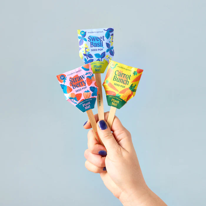 A hand with blue fingernails holds a cute bouquet of three seed pops, showing the strawberry, sweet basil and carrot bunch varieties. It's a fun way to start gardening.