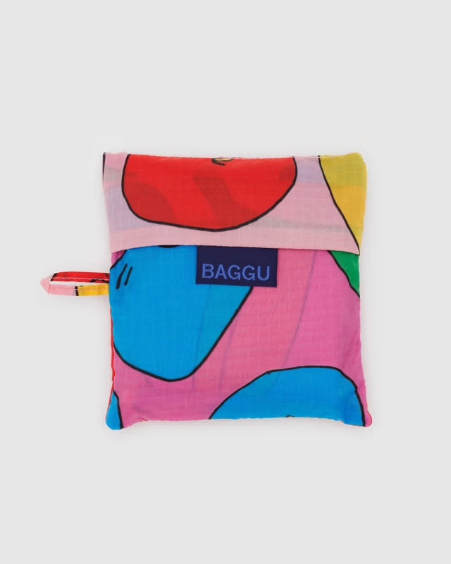 BAGGU reusable tote in bananas and apples print neatly folded into its matching 5" × 5" pouch. Compact, travel-ready, and made from eco-conscious recycled ripstop nylon.