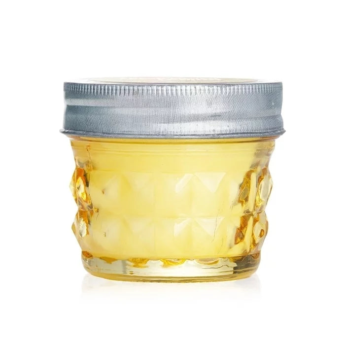 A short, yellow artisan soy wax candle is shown in a clear glass jar with a textured diamond pattern and a silver-colored metal lid.