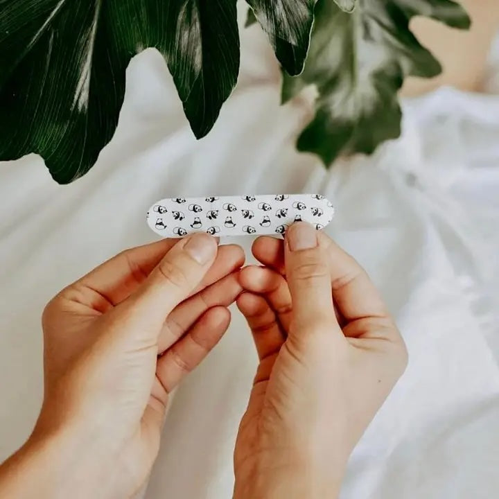 Close-up of an adult’s hands holding a bamboo-fiber bandage strip for kids, on a lifestyle background