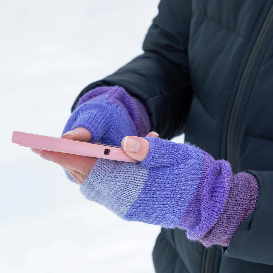 Hands holding a phone while wearing alpaca fingerless mittens in shades of purple. Handmade in Bolivia and gentle on sensitive skin.