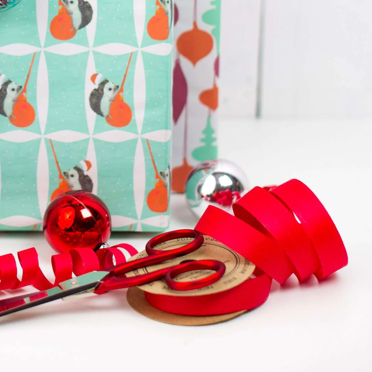 Close-up of vibrant red natural cotton curling ribbon near a wrapped gift, showing its soft texture and eco-friendly water-based dye. Made from 100% cotton yarn and fully compostable.
