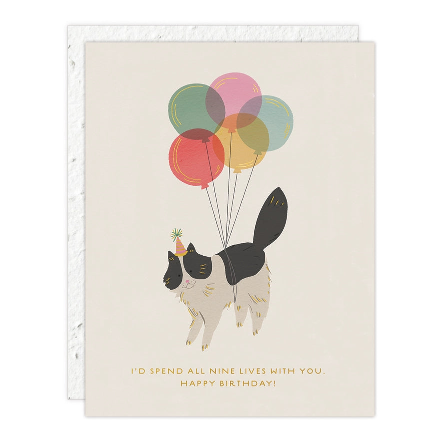 Cute cat with balloons and party hat, gold foil text "I’d spend all nine lives with you. Happy Birthday!" on a seed paper greeting card.