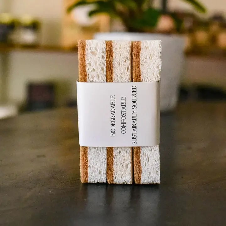 A pack of three natural sponges stacked in a kitchen setting, emphasizing their quick-dry, biodegradable, and non-abrasive qualities.
