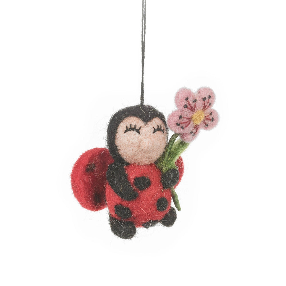 A handmade felt ladybug holding a pink flower is shown. It has a black body and head with red wings that have black spots.