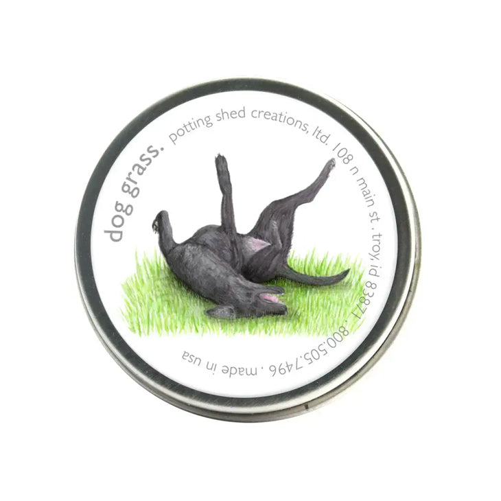 A silver tin of garden sprinkles with a white label on the lid. The label features a watercolor illustration of a black dog rolling playfully on its back in green grass, with the text 'dog grass, potting shed creations' around the edge.