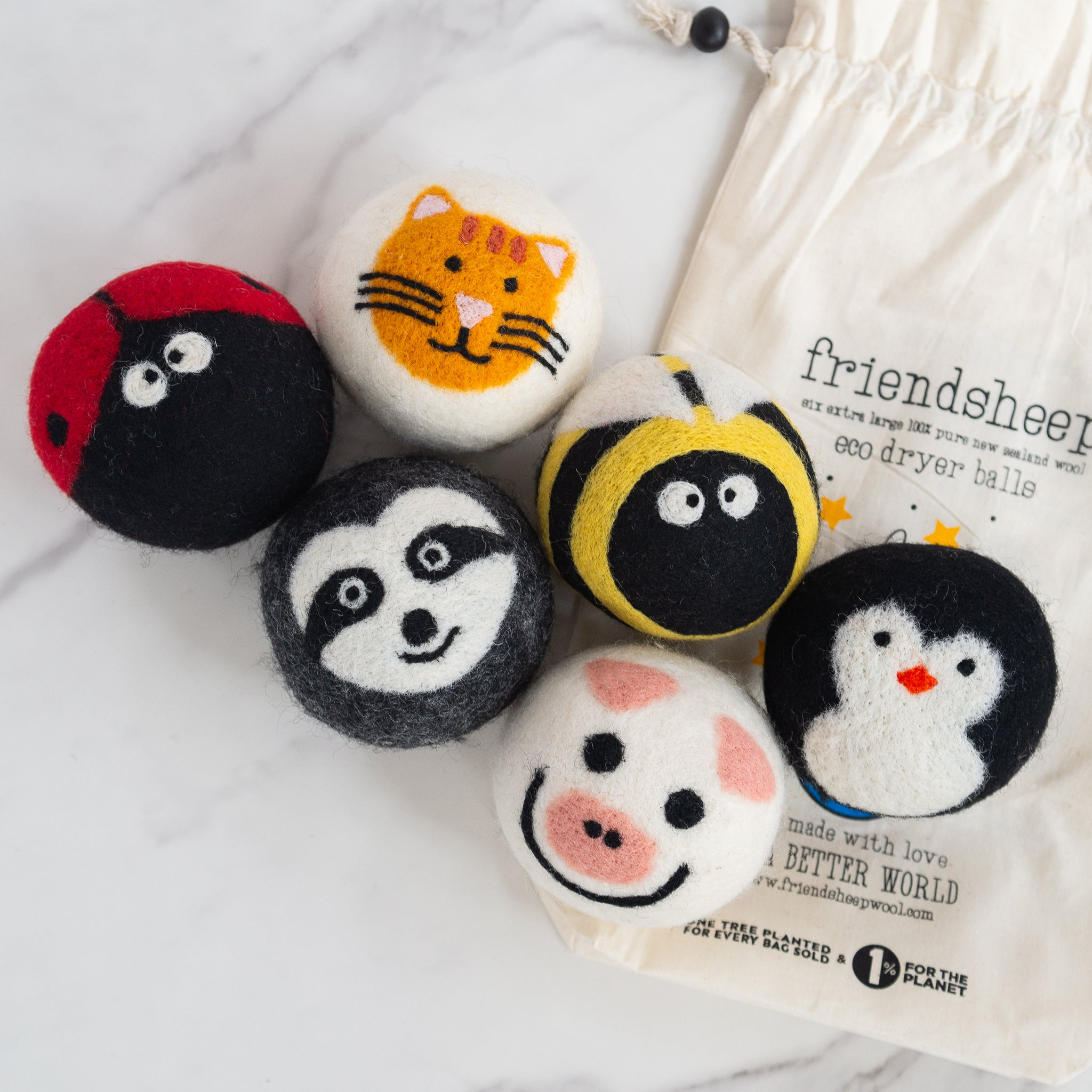 Top view of eco-friendly Critter Camp wool dryer balls collection on a white marble surface, featuring animal designs including pig, penguin, bee, cat, ladybug, and raccoon.
