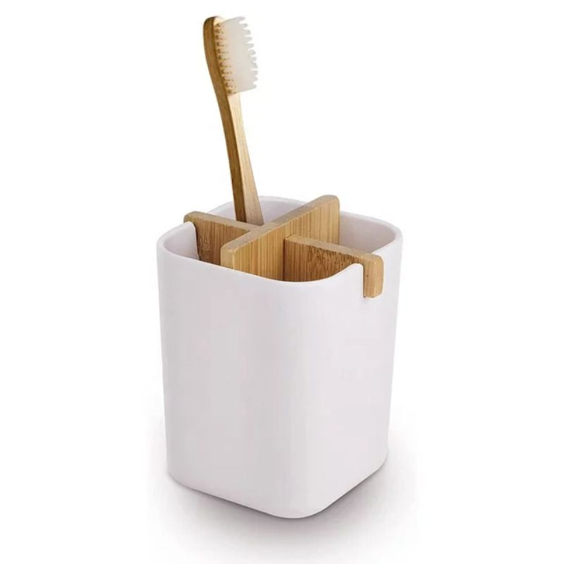 A rectangular white toothbrush holder with a bamboo cross-shaped divider. One compartment holds a bamboo toothbrush with white bristles.