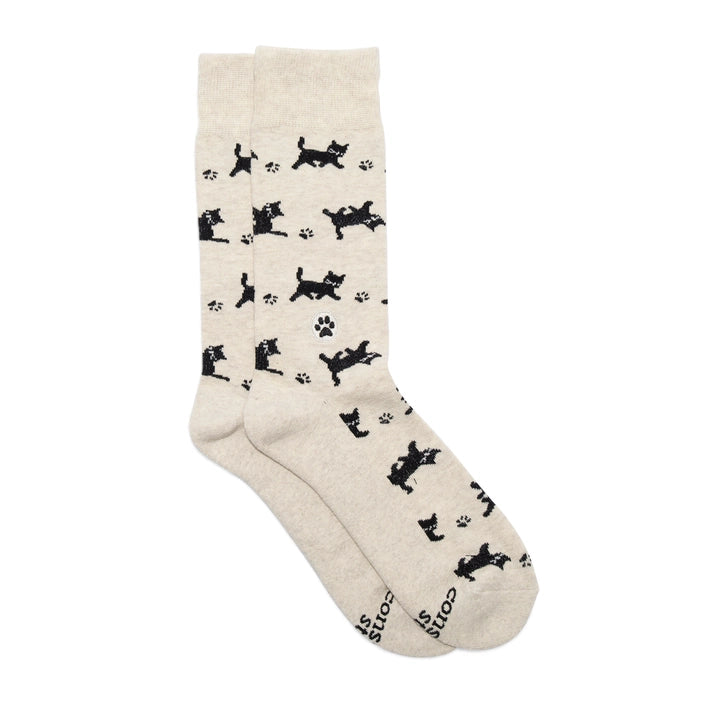 A pair of light-colored Conscious Step socks with a pattern of black cats and paw prints is shown against a white background. The brand name is visible on the bottom of the socks.