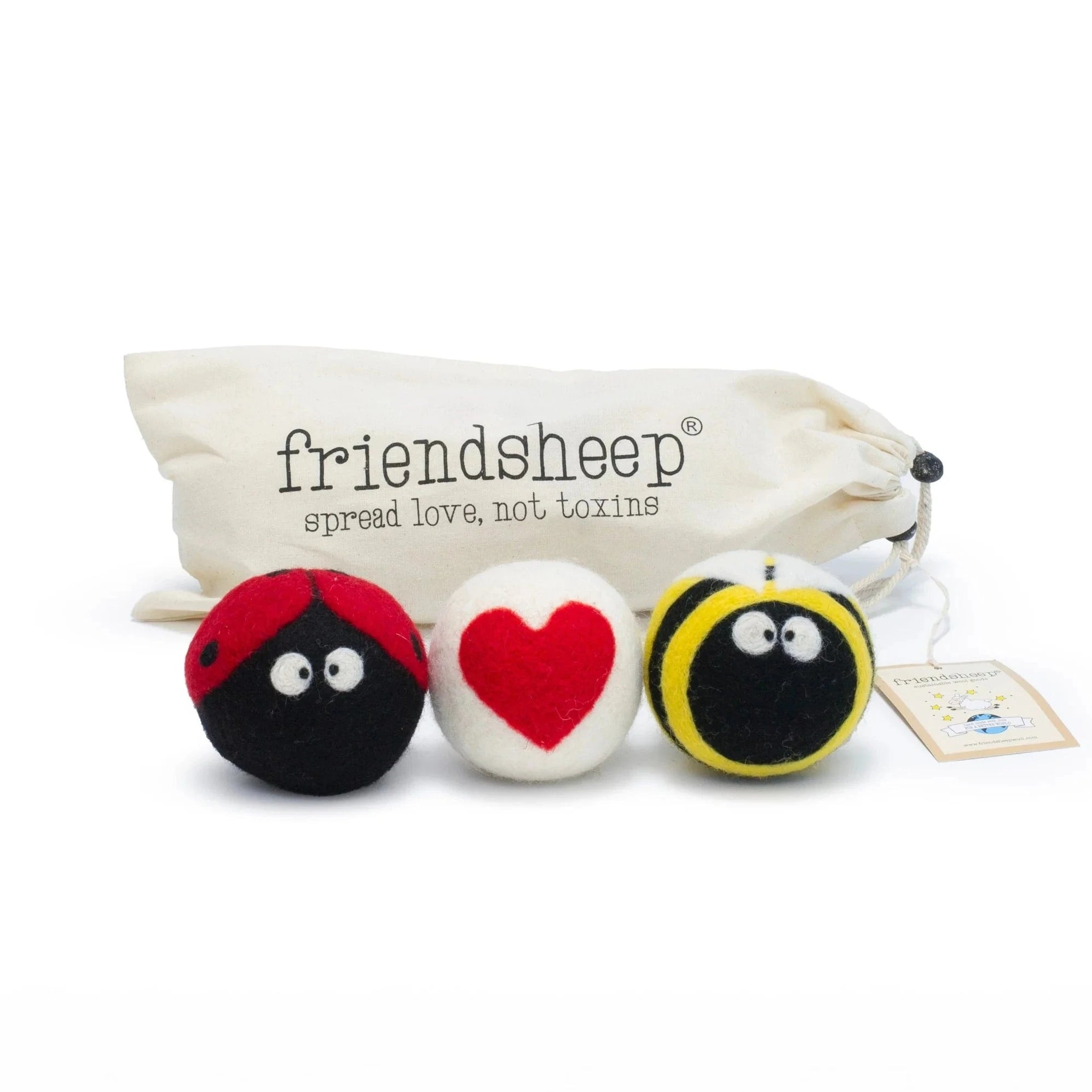 A set of three Friendsheep sustainable goods wool dryer balls are shown decorated with a cute ladybug, a red heart and a bee. They are sitting in front of their white canvas drawstring bag.