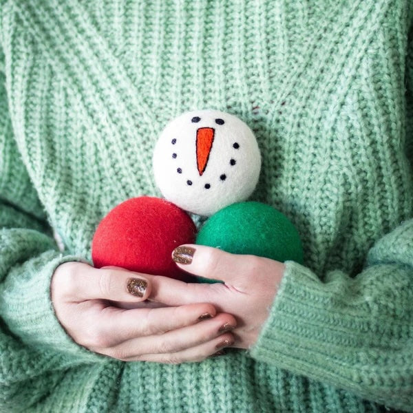 Woman holding three holiday dryer balls; a snowman, a red and a green wool ball.