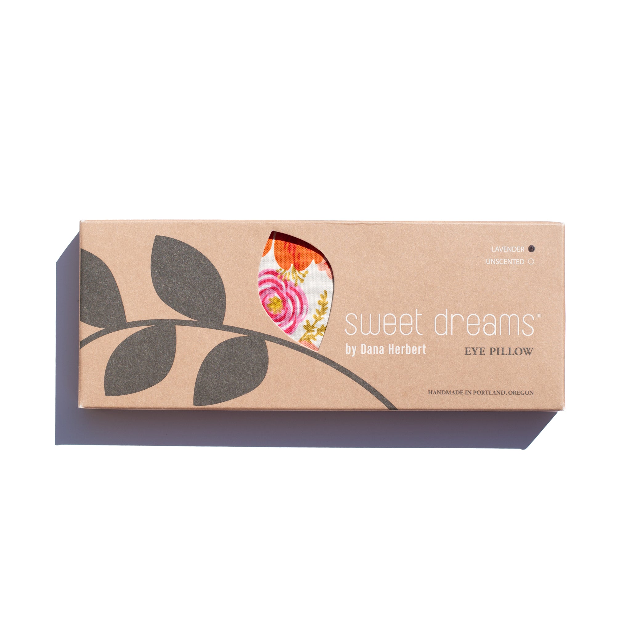 A cardboard box for a "sweet dreams" eye pillow by Dana Herbert is on a white background. A cutout shows a glimpse of the floral-patterned pillow inside. The box notes lavender is an ingredient.