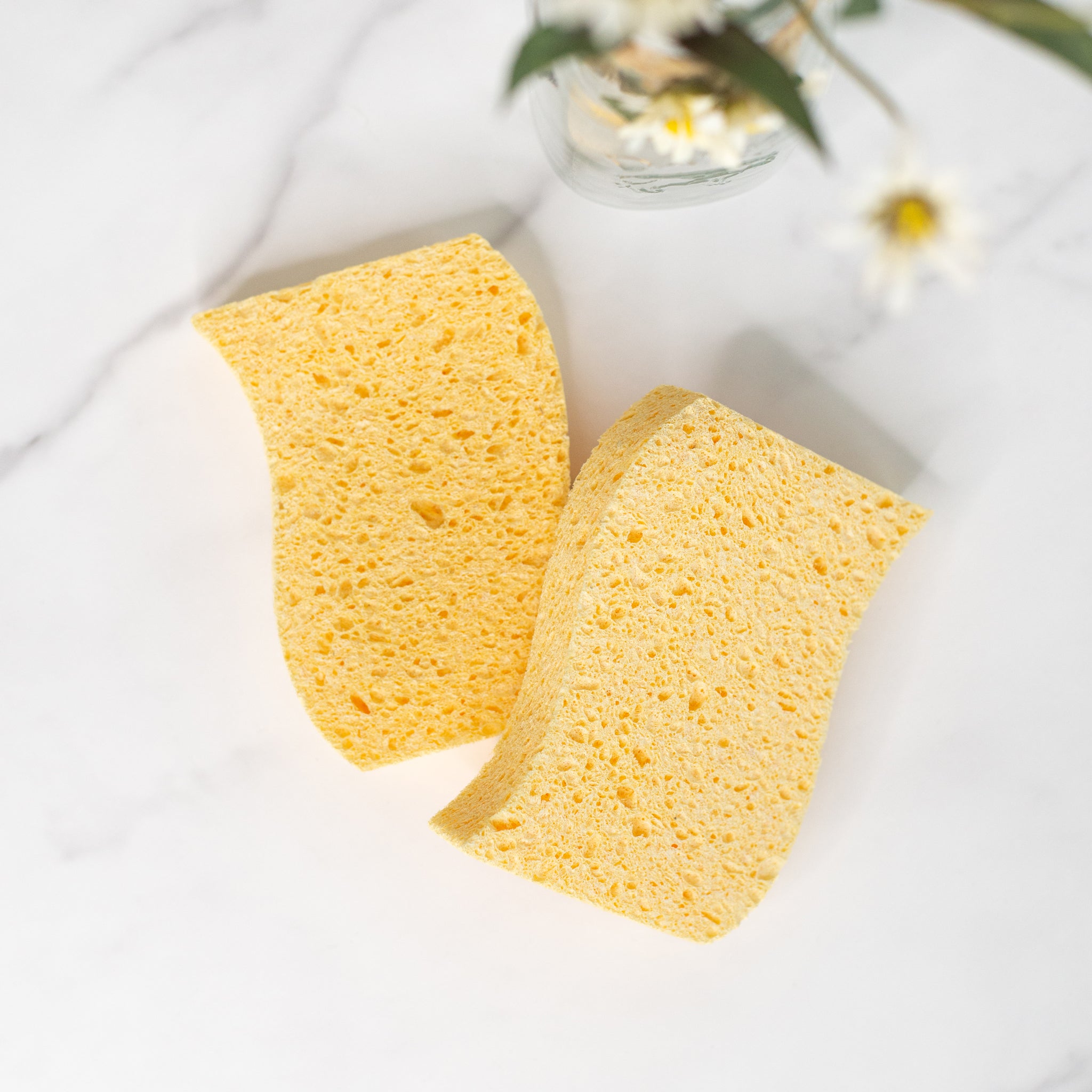Close-up of two natural plant cellulose biodegradable kitchen sponges in a marble surface with some white flowers.