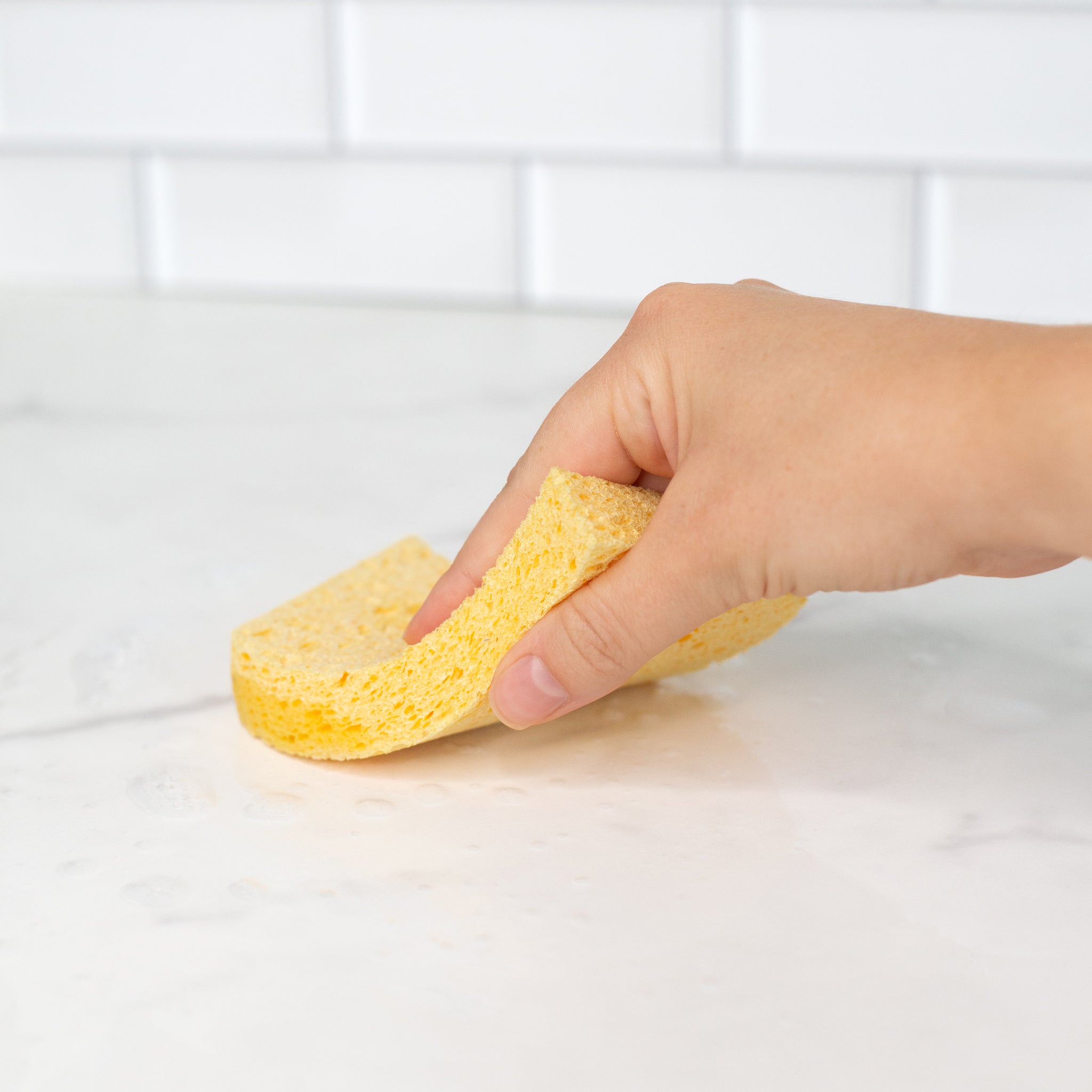 A hand usieng a natural plant cellulose biodegradable kitchen sponges in a marble surface.