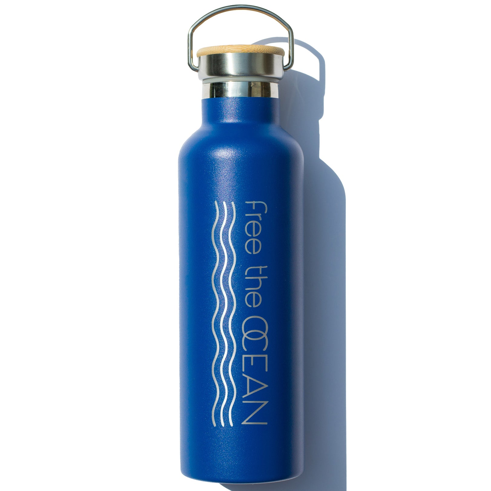 A matte blue reusable water bottle with a bamboo lid and metal handle. It has the words "Free the OCEAN" and two wavy lines in white on the side.