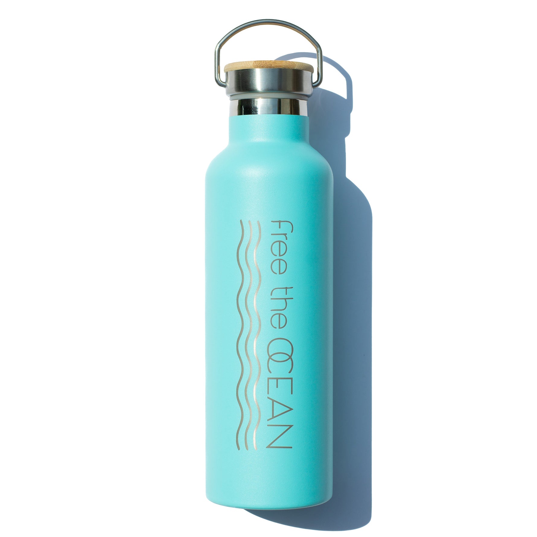 A light blue metal reusable water bottle with a bamboo lid and a metal handle. The words "free the OCEAN" are printed vertically on the side.