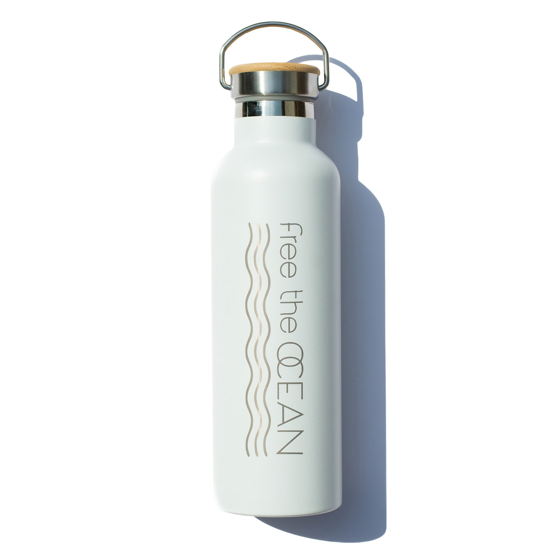 A white metal water bottle with a bamboo lid and a metal handle. The text 'free the OCEAN' is printed vertically on the side.