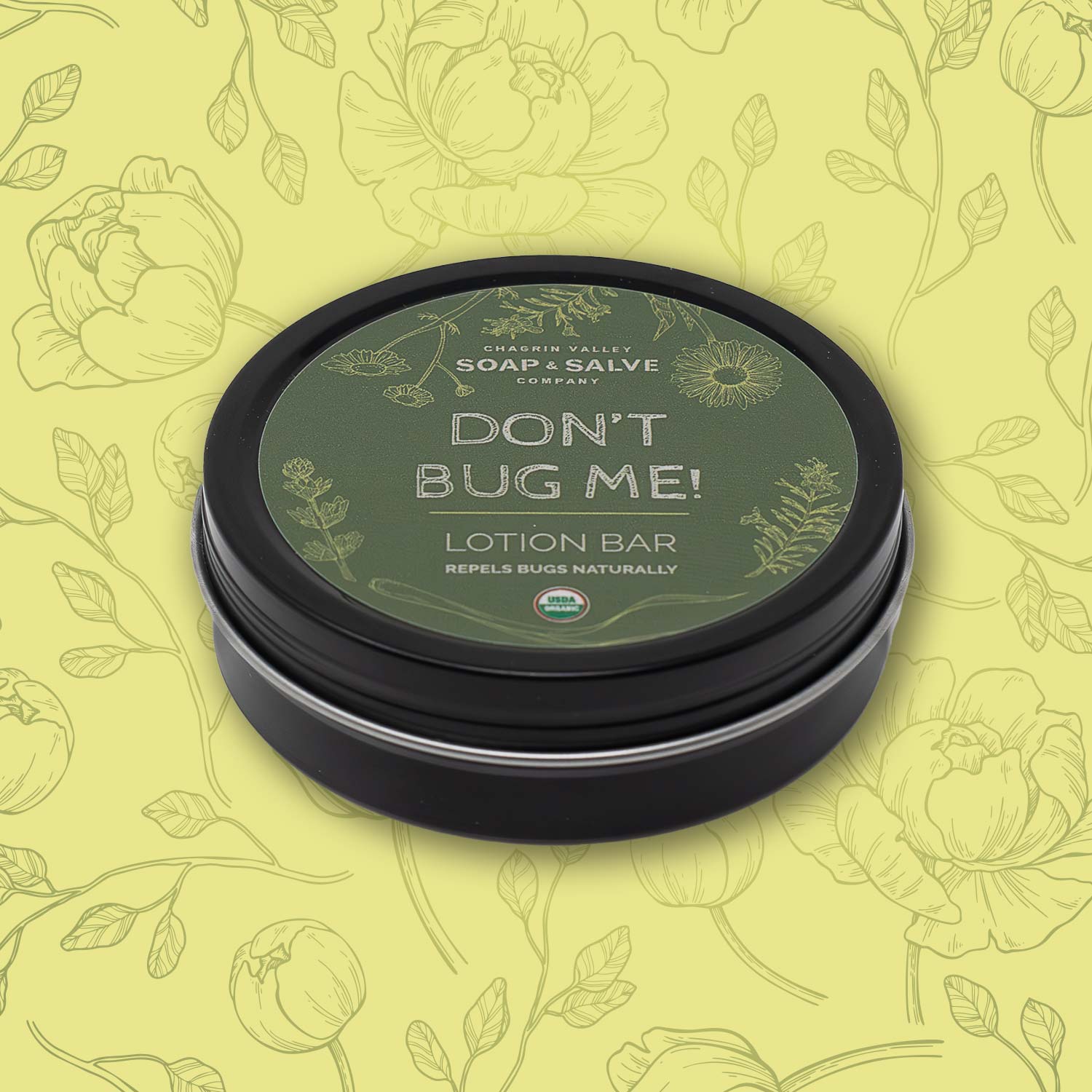 A round, closed black tin of 'Chagrin Valley Soap & Salve Company' 'Don't Bug Me!' Lotion Bar. The label also states that it "repels bugs naturally" and includes a small "USDA Organic" logo.