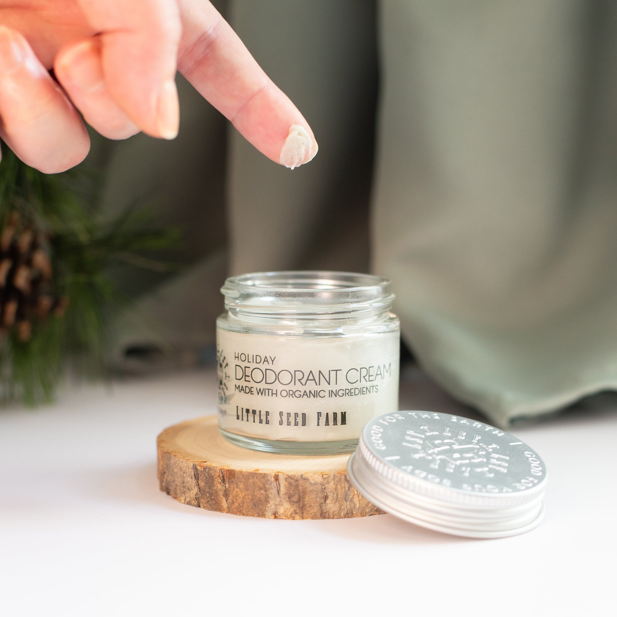 A finger has scooped some Little Seed Farm Holiday deodorant cream from a jar, ready for application.
