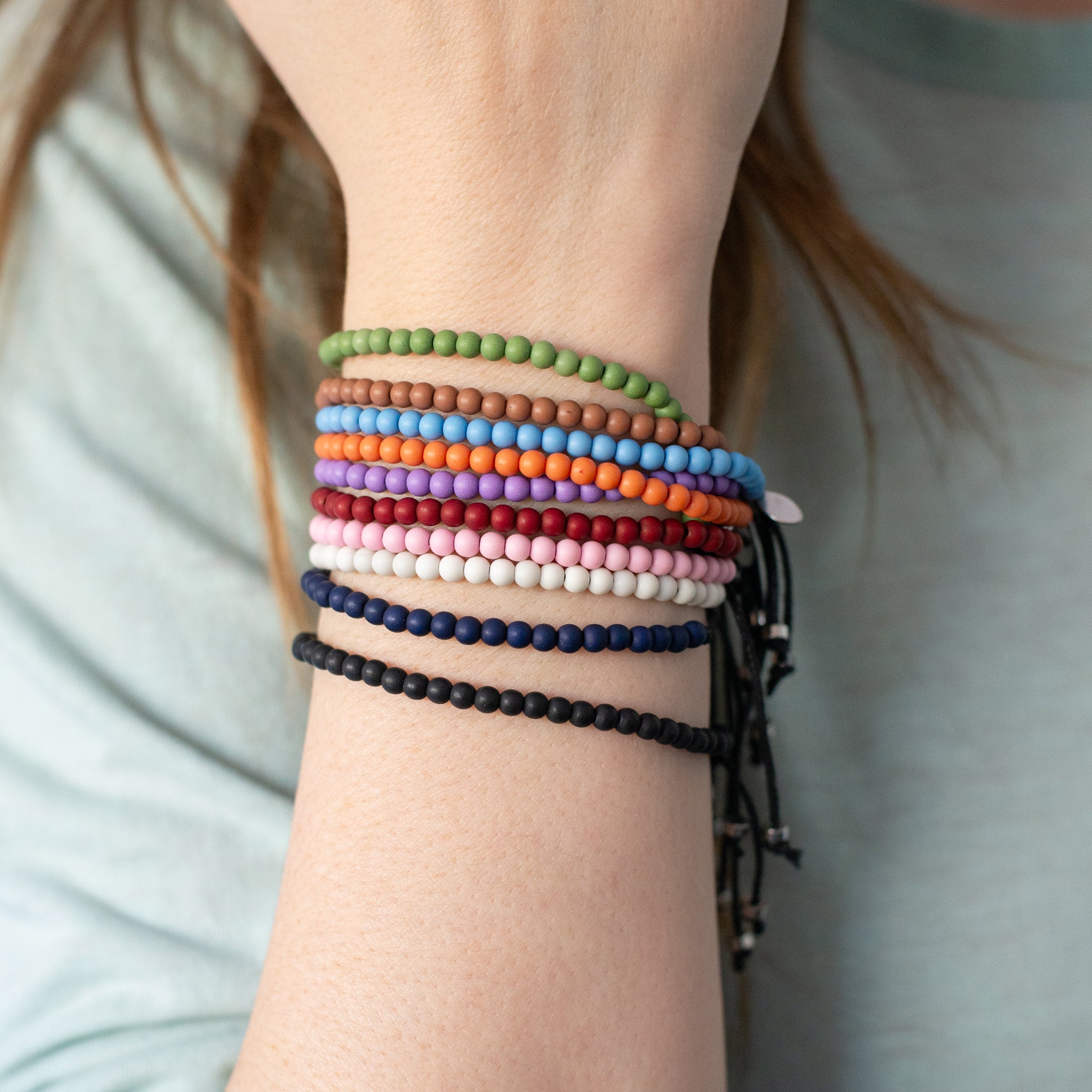 Wrist wearing multiple color recycled ocean plastic bracelets. Durable, adjustable, and handmade in Bali—each purchase removes one pound of trash from waterways.