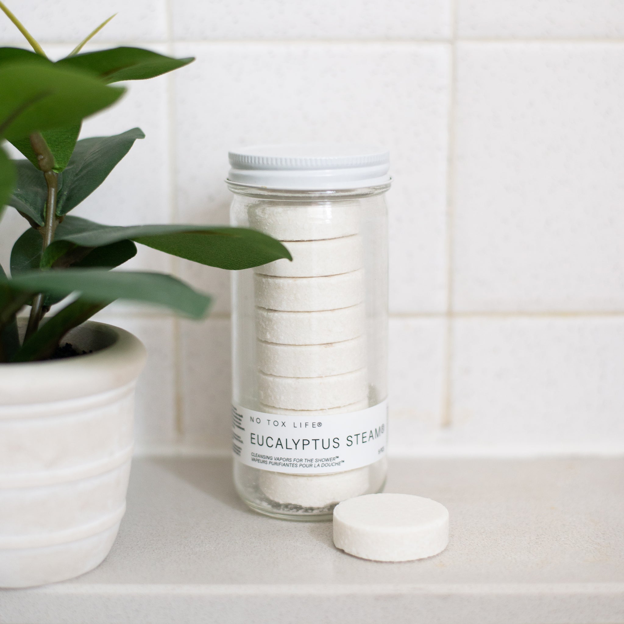 A glass jar of 'No Tox Life' Eucalyptus Steams. The jar contains eight stacked, white cleansing vapors, and a single round vapor disc sits in front of it.