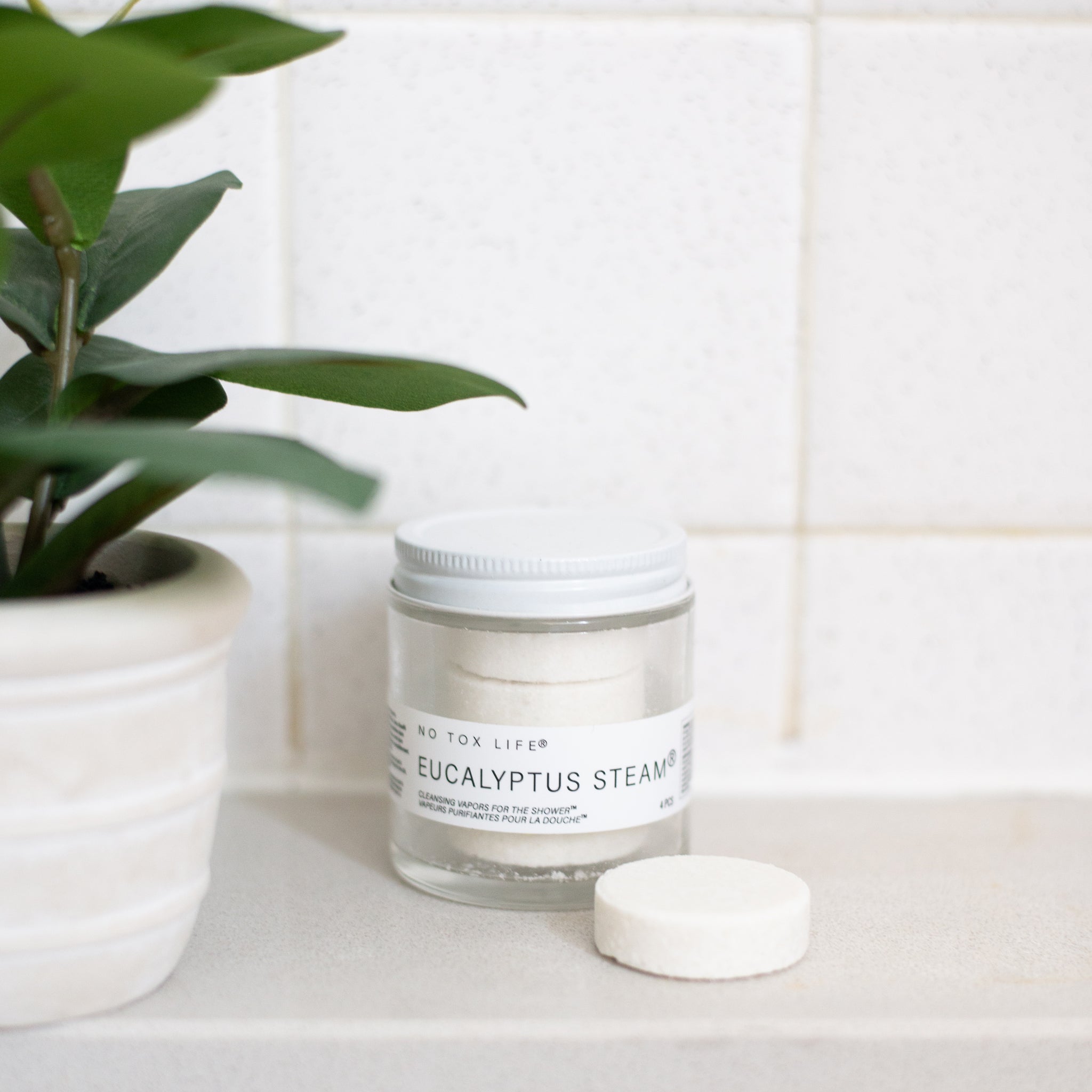 A glass jar of 'No Tox Life' Eucalyptus Steam, with a white lid and four white, round cleansing vapors stacked inside. One single vapor disc sits in front of the jar.