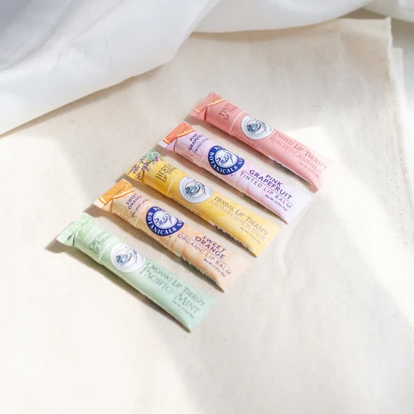 A collection of organic lip therapy balms in flavors like Pink Grapefruit, Strawberry Watermelon, and Pacific Mint—handcrafted with botanical butters and oils, and packaged in home-compostable tubes.