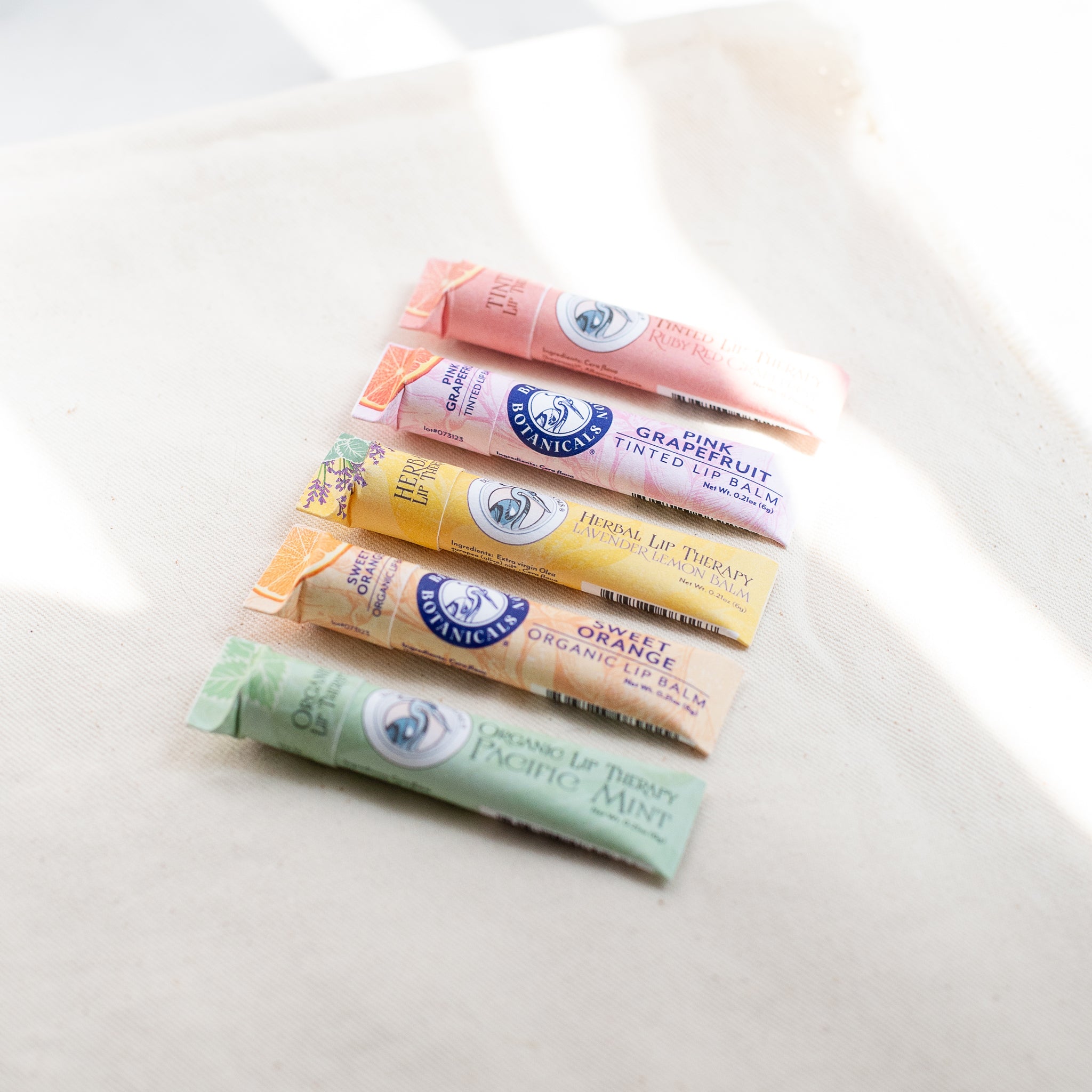 An assortment of nourishing lip balms, including Vegan Pacific Peppermint, Lavender Lemon, and Coastal Berry, each made with ethically sourced ingredients and wrapped in 100% recycled paperboard.