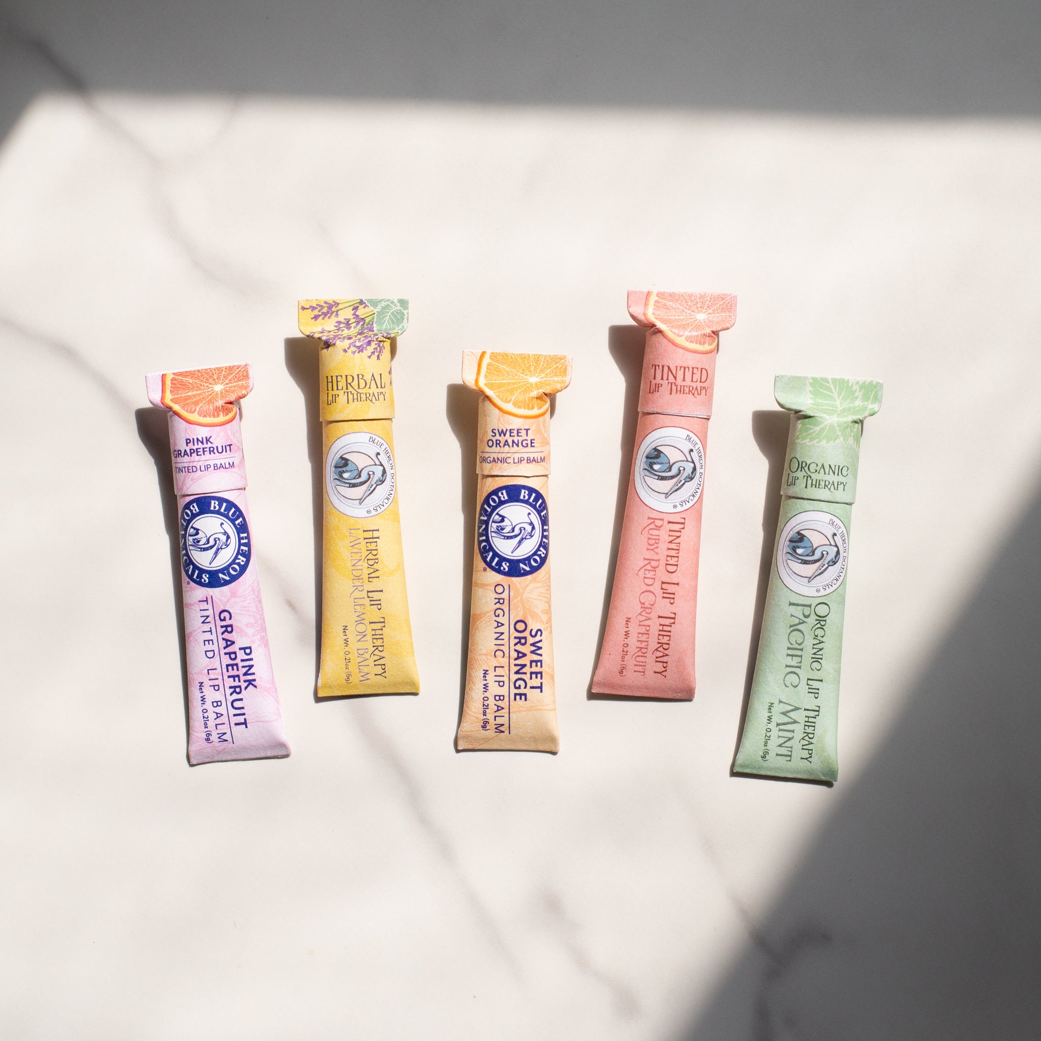 A vibrant display of eco-friendly lip therapy balms, featuring Sweet Orange, Vegan Pacific Peppermint, and Pink Grapefruit—formulated to hydrate and protect lips with organic, cruelty-free care.