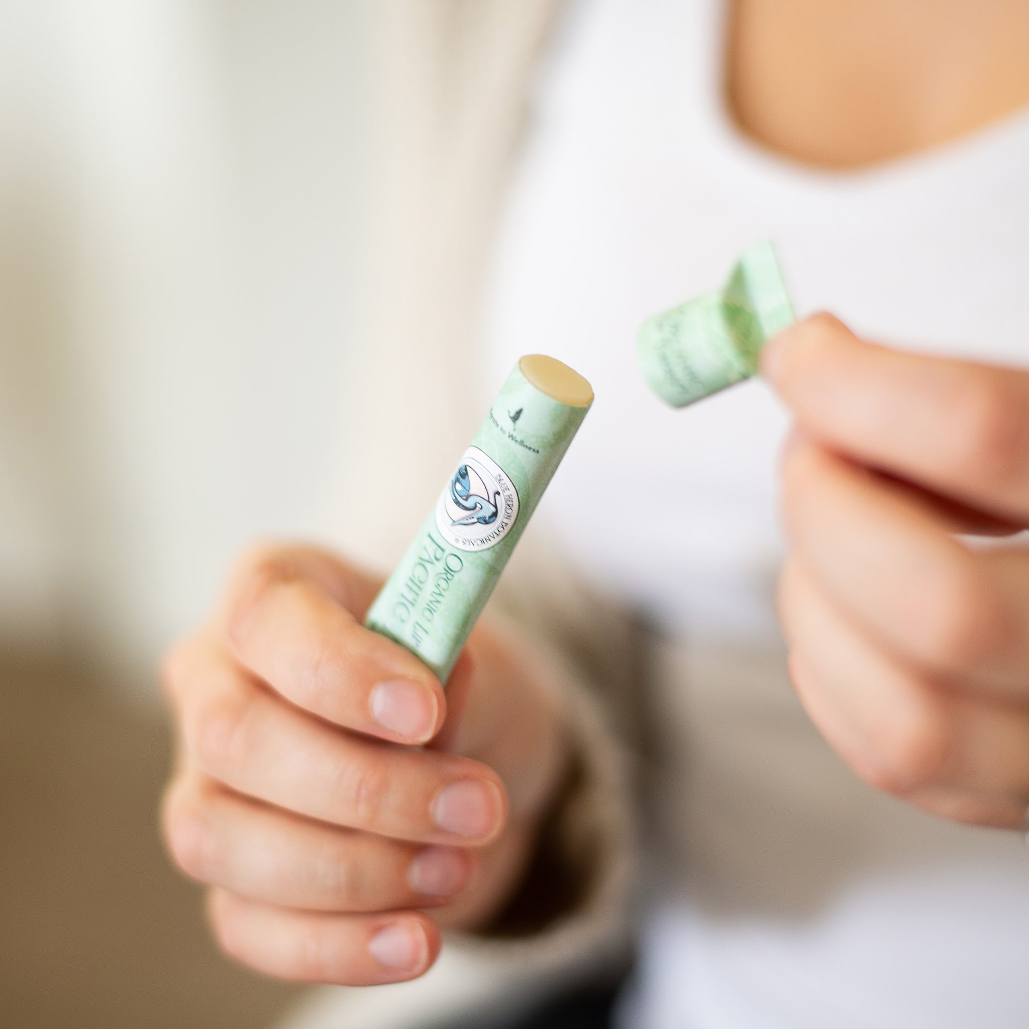 Person holding a Pacific Mint Lip Therapy Balm tube, with soft natural light highlighting the clean, minimal setting. Made with organic ingredients and packaged in compostable, plastic-free paperboard.
