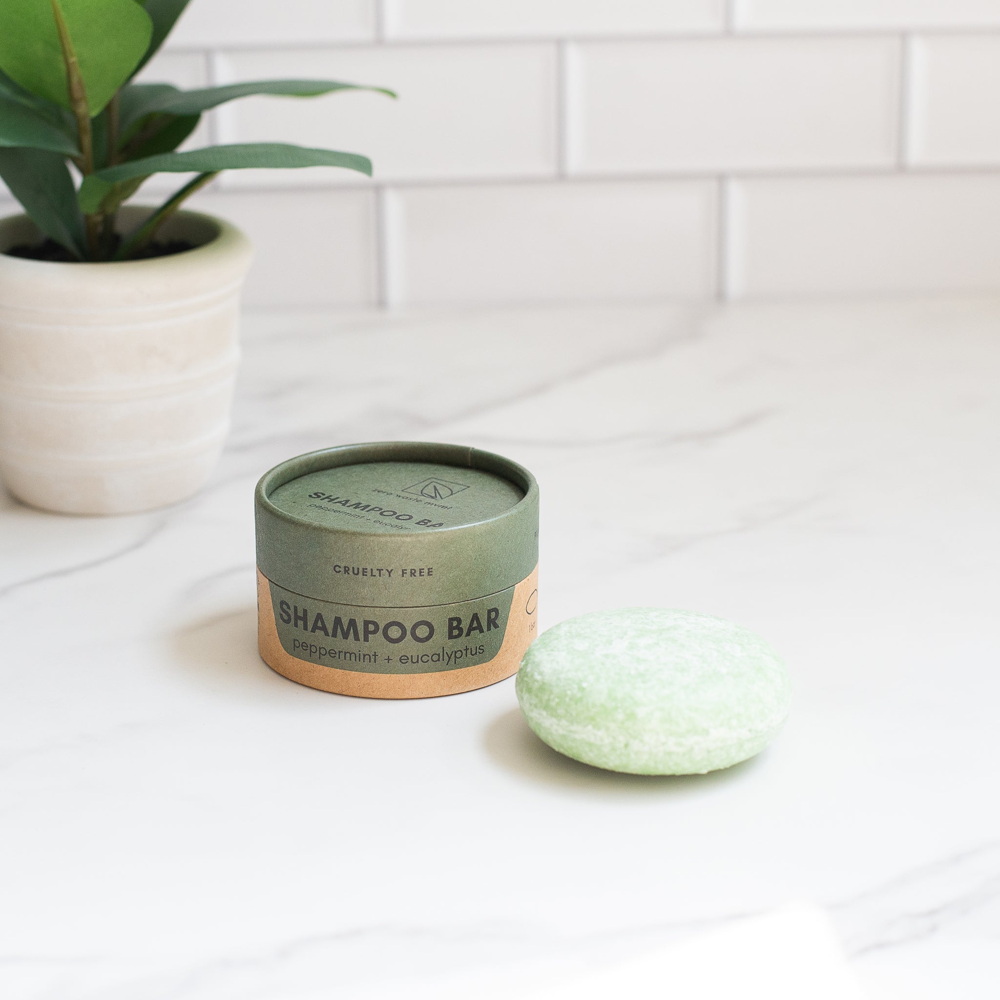 A "CRUELTY FREE" shampoo bar rests next to its "peppermint + eucalyptus" container. The speckled green oval bar is ready for use.