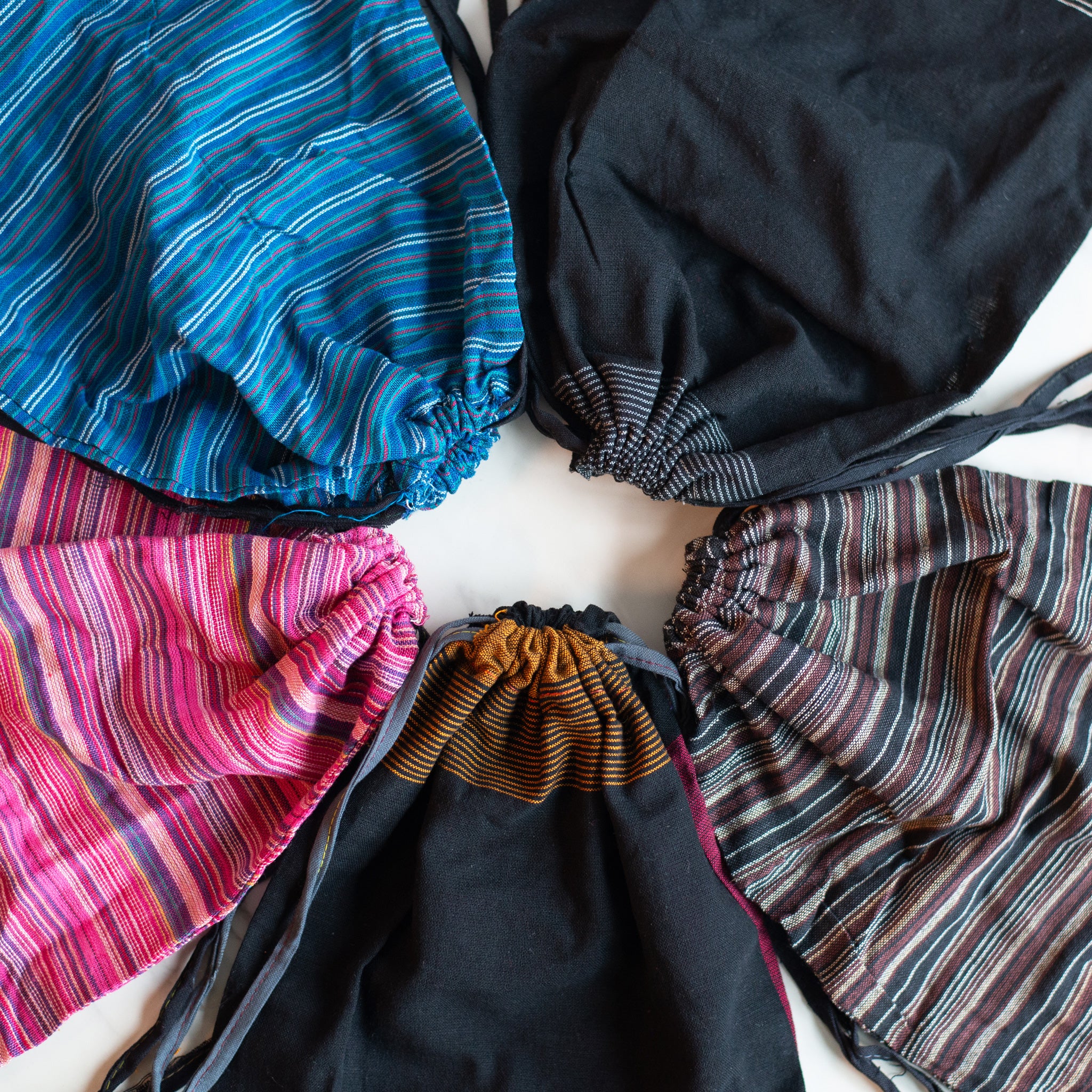 A variety of recycled drawstring bags in vibrant striped and solid fabrics, laid out in a circle to showcase eco-friendly design options.