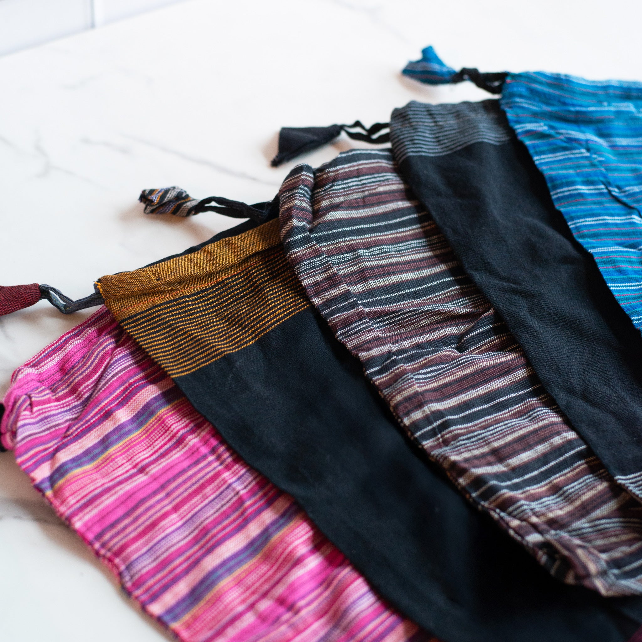 A row of colorful recycled drawstring bags in various striped patterns, highlighting their eco-friendly materials and unique designs.