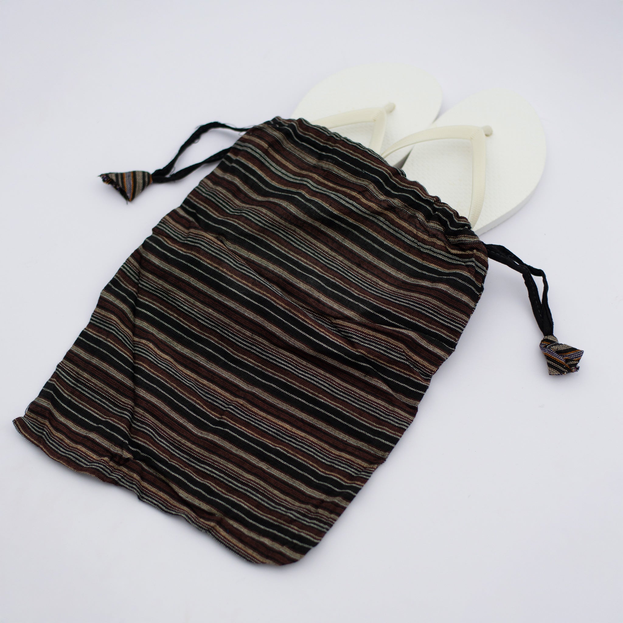 A brown and black striped recycled drawstring bag holds a pair of white flip-flops, highlighting its usefulness for travel or beach outings.