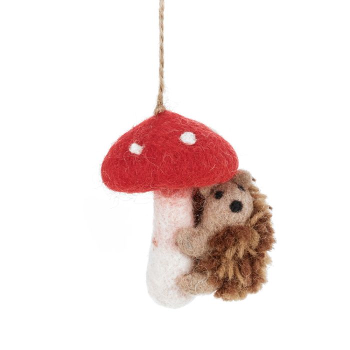 A handmade felt hanging ornament of a fuzzy hedgehog hugging a red mushroom with white spots is shown.