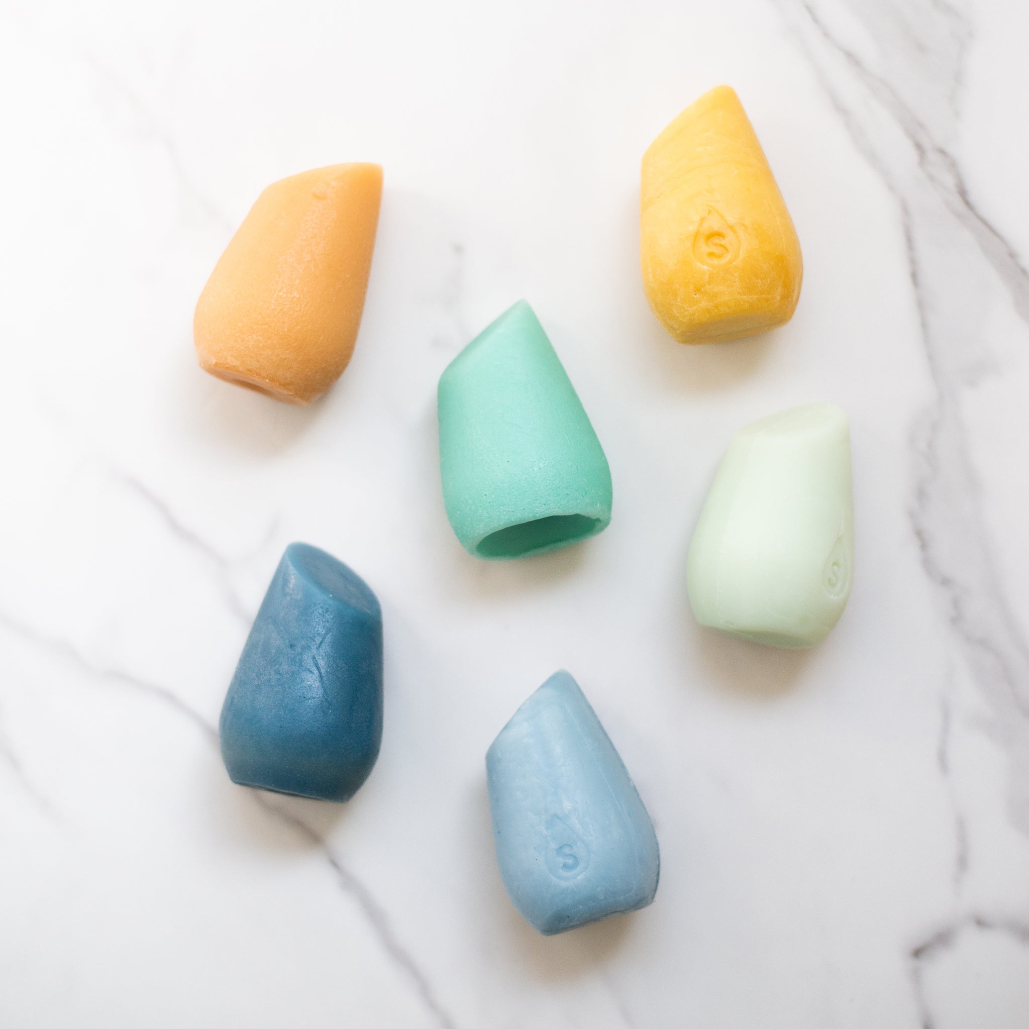 An array of the HiBar MOISTURIZE solid shampoo and conditioner tear-drop bars in different colors, featuring light tangerine, green, mango yellow, deep blue, light blue and light green