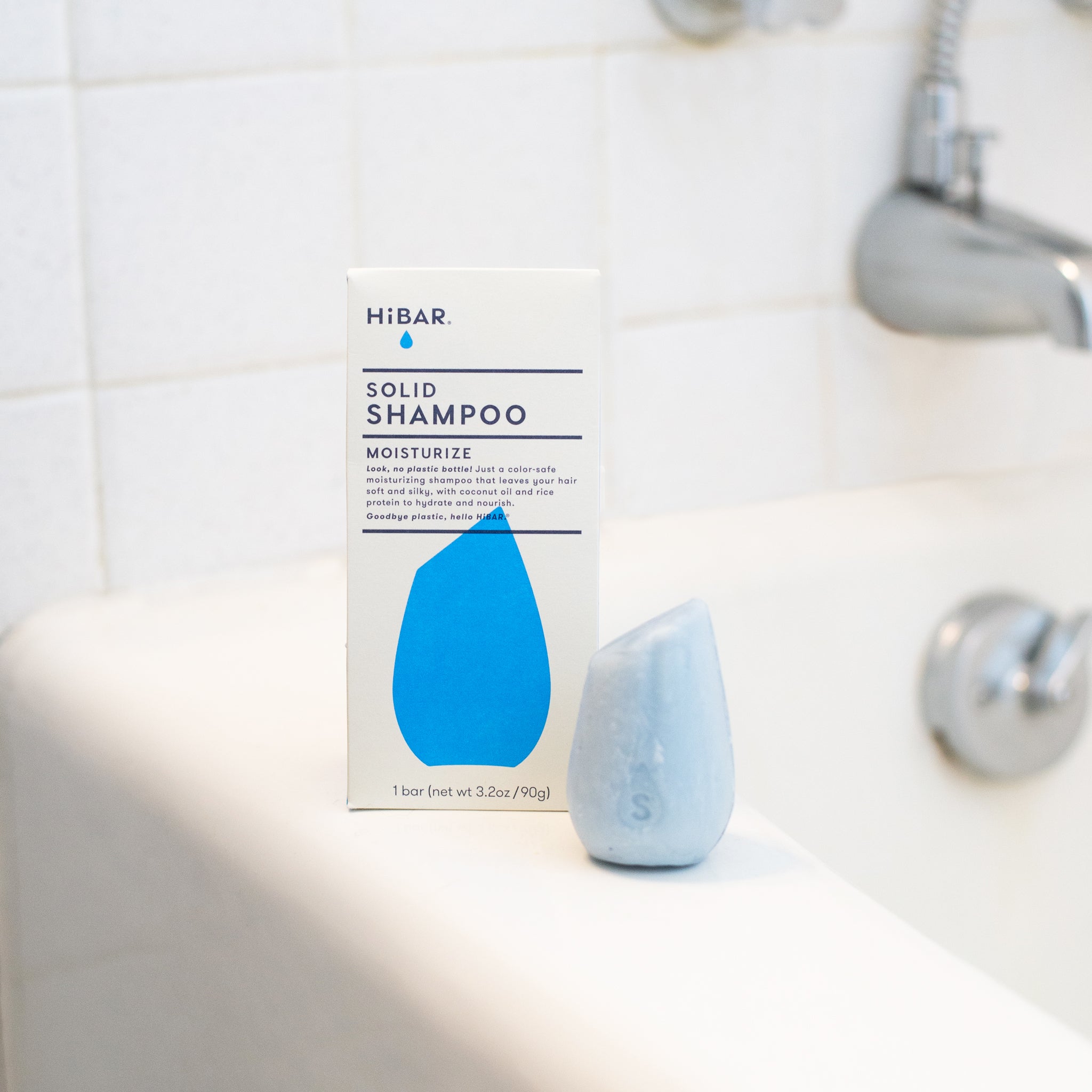 HiBar MOISTURIZE Solid Shampoo bar, light blue and tear-drop shaped with an 'S' pressied on it, highlights the product's plastic-free design, coconut oil, and rice protein ingredients.