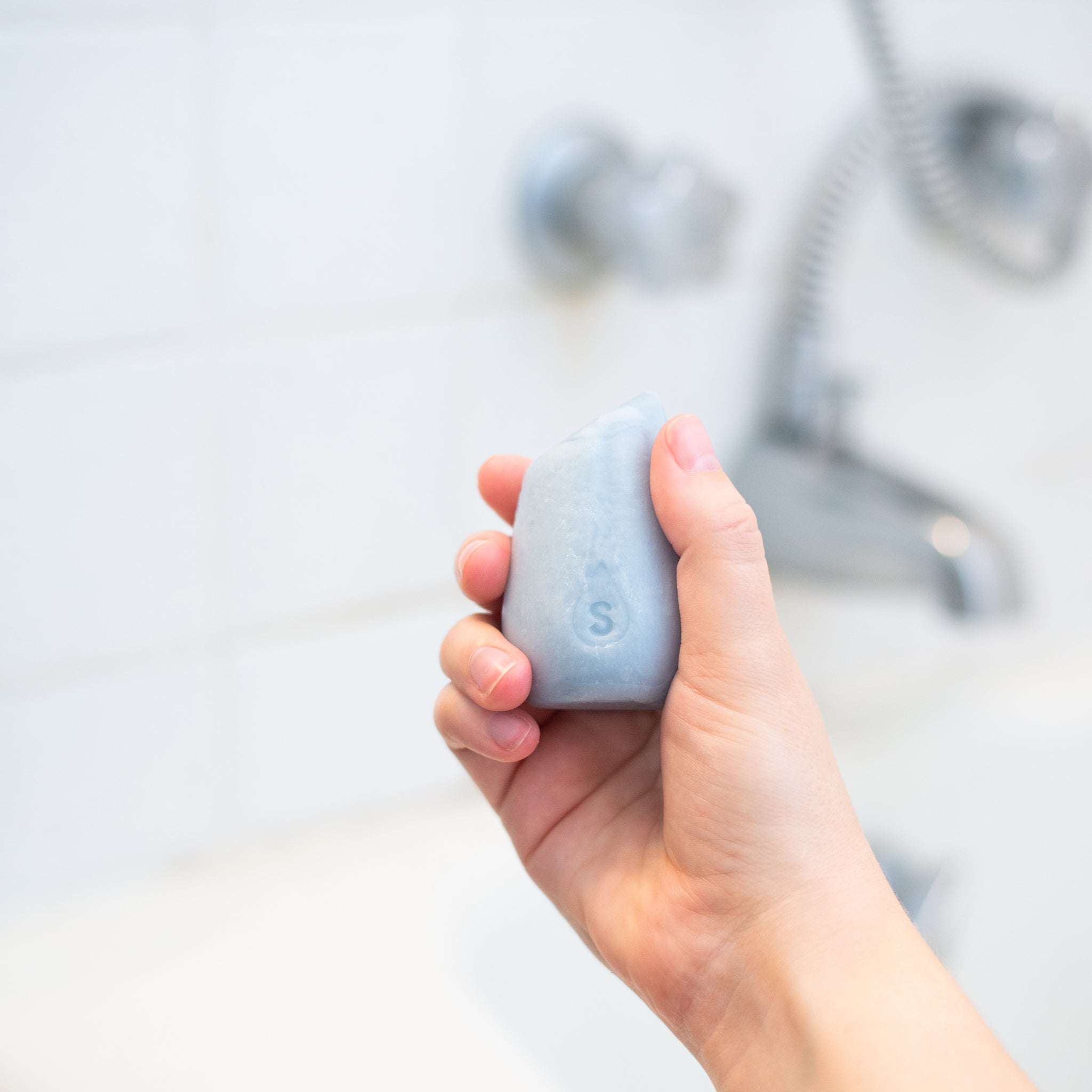 A hand holding the HiBar MOISTURIZE tear-drop shaped solid shampoo bar, made easy to handle