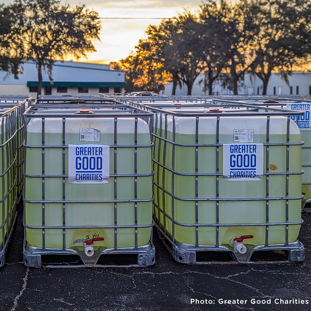 Large water containers labeled “Greater Good Charities” are lined up for disaster relief efforts at sunset. Photo by Greater Good Charities.