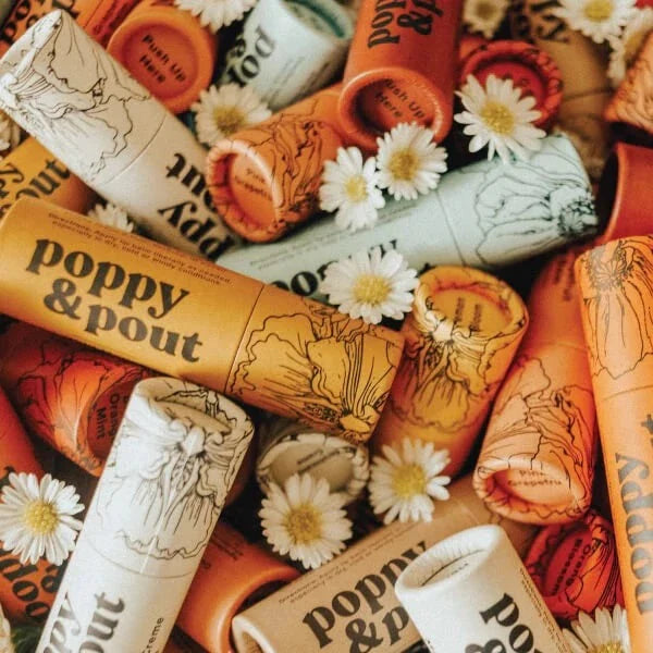 Top-down view of several Poppy & Pout lip balm tubes with daysies.