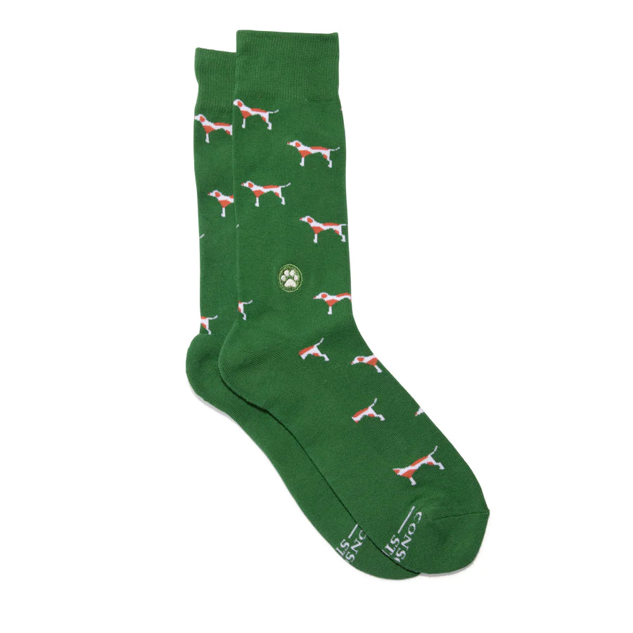 A pair of green socks with a pattern of red and white dogs is shown against a white background. The brand name is visible on the bottom of the socks.