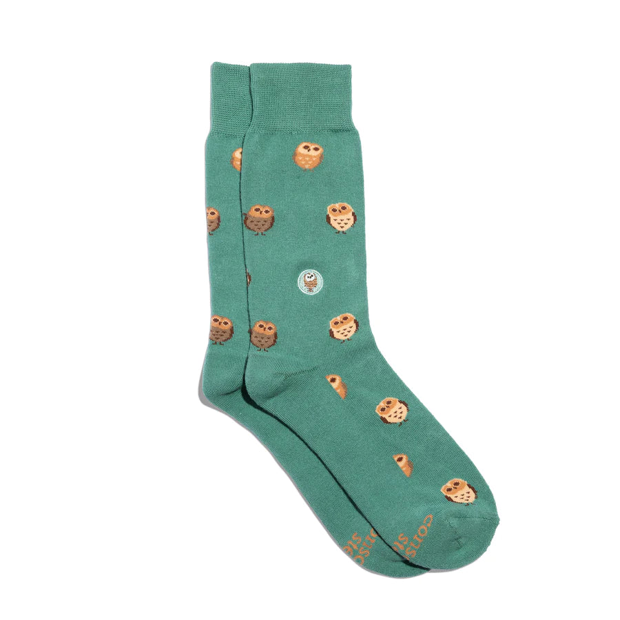 A pair of green Conscious Step socks with a pattern of owls is shown against a white background. The brand name is visible on the bottom of the socks.