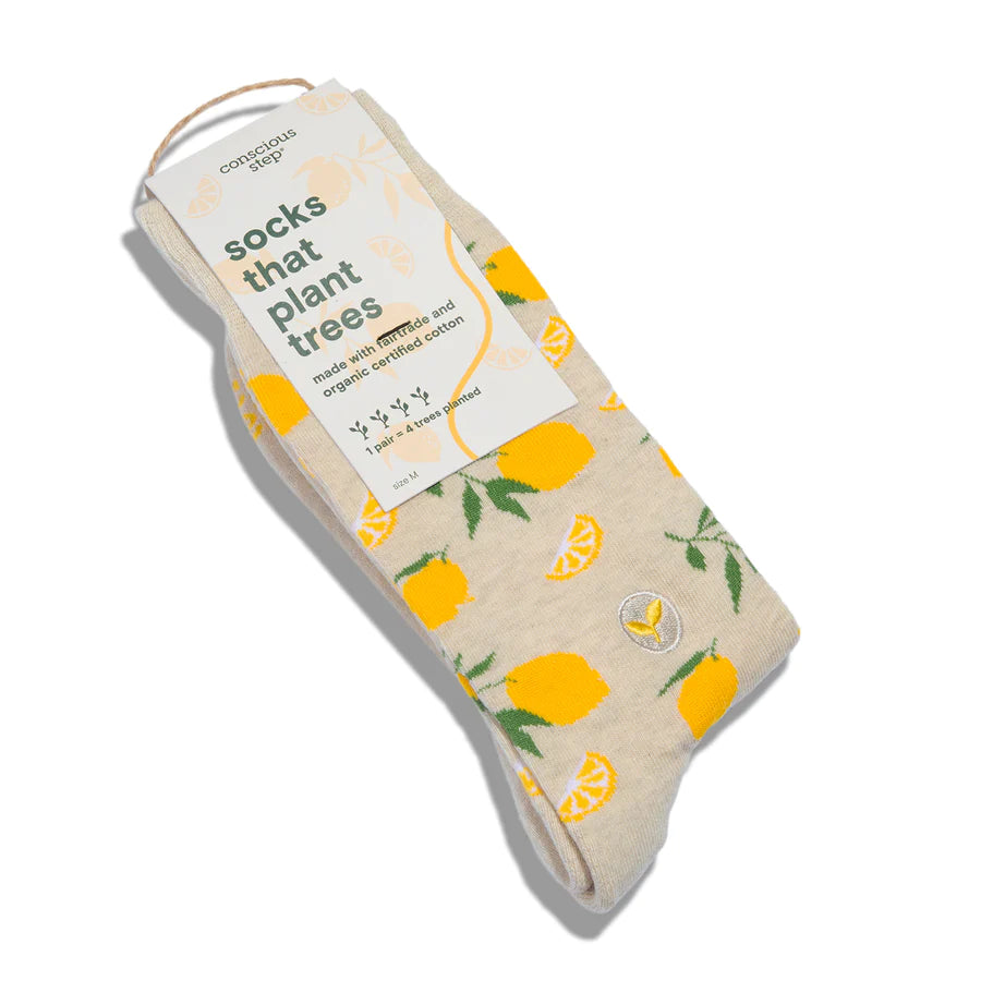 A pair of Conscious Step socks with a lemon and leaf pattern is shown with its tag. The tag states they are "socks that plant trees," made with fairtrade and organic cotton, with "1 pair = 4 trees planted".
