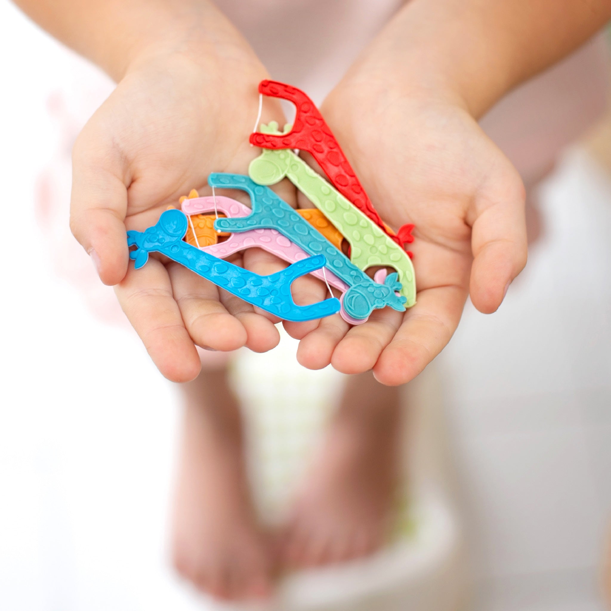 A cute handful of colorful, giraffe-shaped kid's floss picks in red, green, blue and pink. The fun shapes are held out, showing the variety of colors and designs.